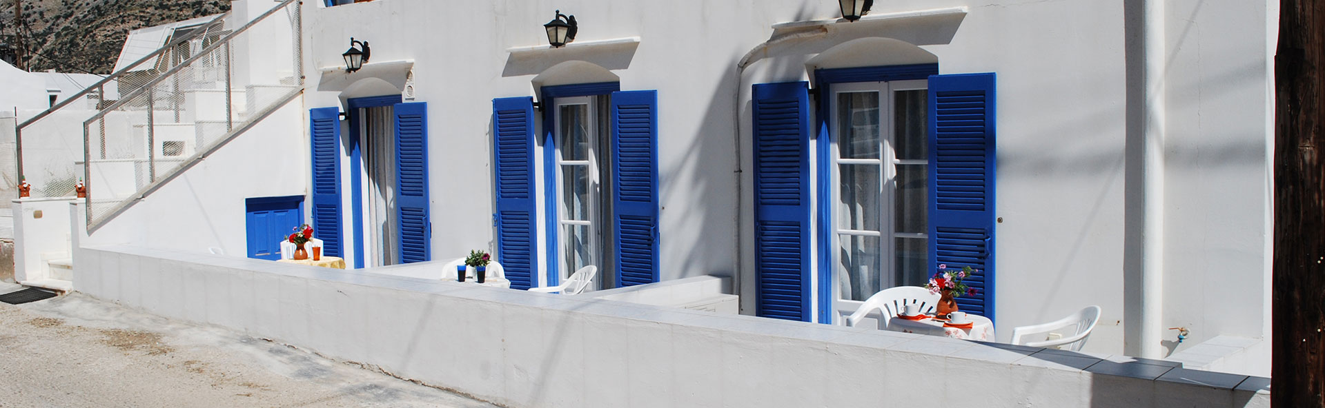 Vue extérieure des chambres To Steno à Kamares, Sifnos, avec volets bleus et terrasse extérieure